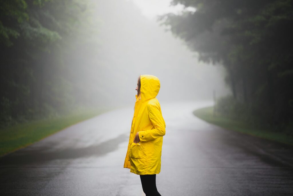 Person in yellow raincoat standing in misty rain — stylish monsoon fashion