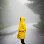Person in yellow raincoat standing in misty rain — stylish monsoon fashion